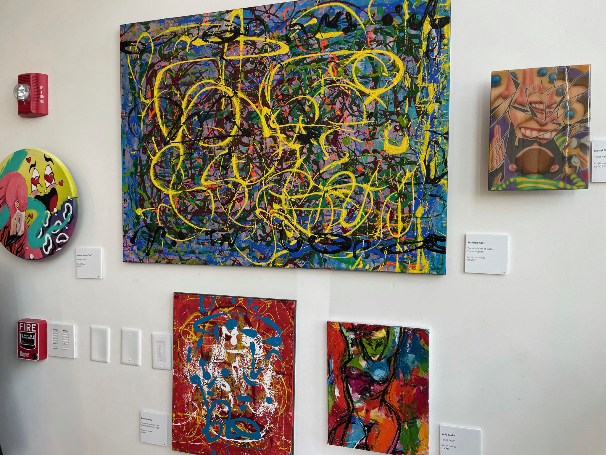 A painting with a yellow line drawing over splatter on a white wall, flanked by smaller works.