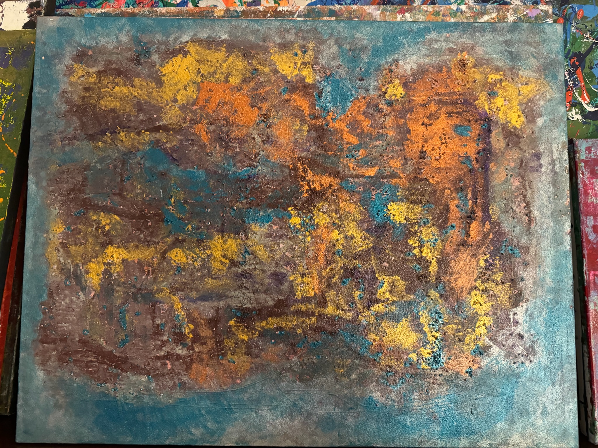 A horizontal painting in teal washes with amber and ochre incursions across the center.